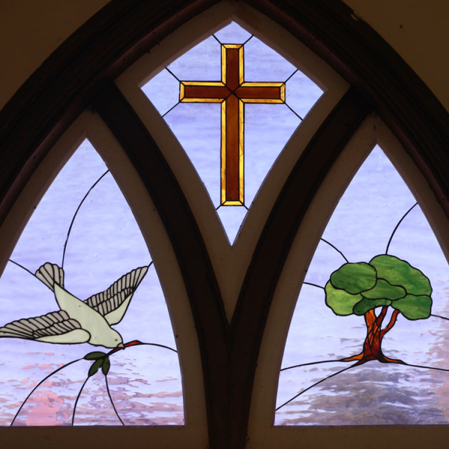 Stained glass window with dove, cross, and tree depicting faith and peace